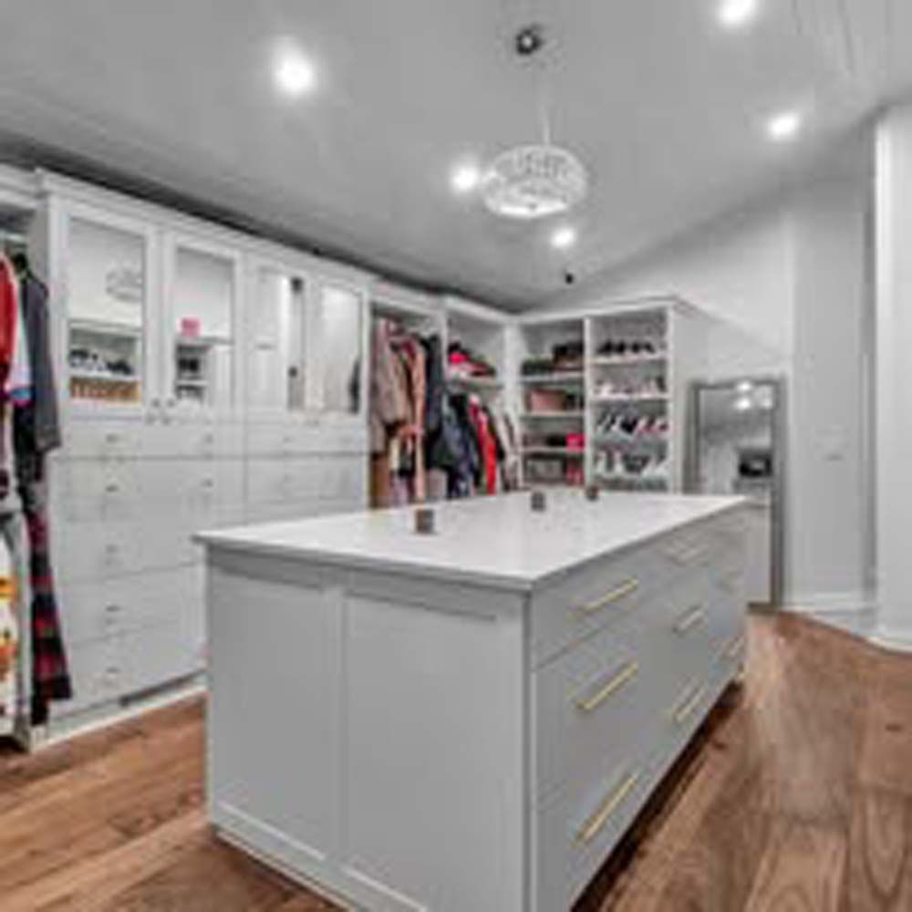 Walk-in closet with white cabinets, island, and wooden floors.