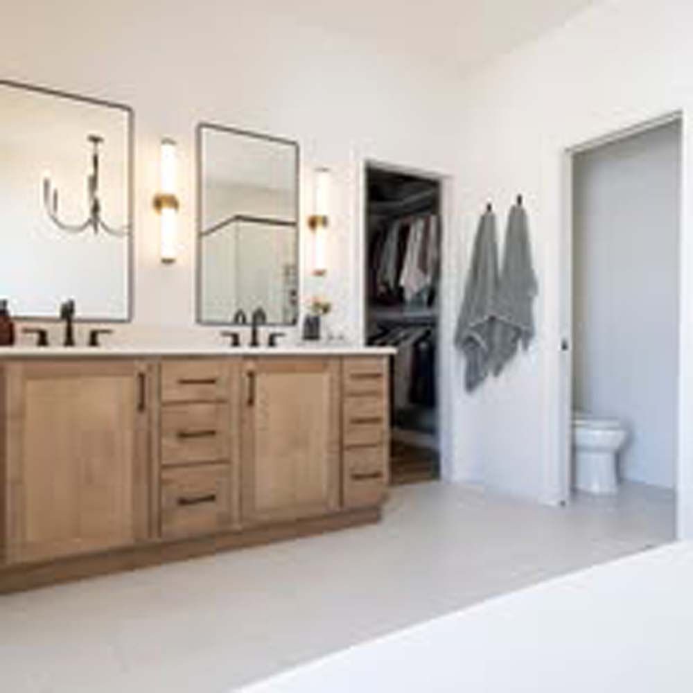 Bathroom with double vanity, mirrors, and open closet. Beige cabinets, white walls, and a toilet.