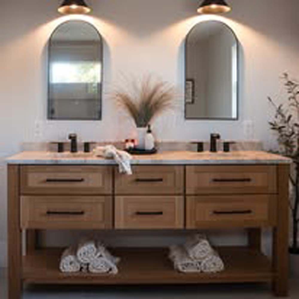 Wooden double sink vanity with arched mirrors, lit by sconces, white towels, decorative sprigs.