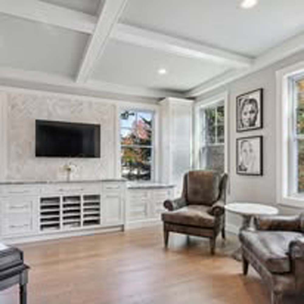 Living room with TV, white built-ins, leather chair, wood floor, windows.