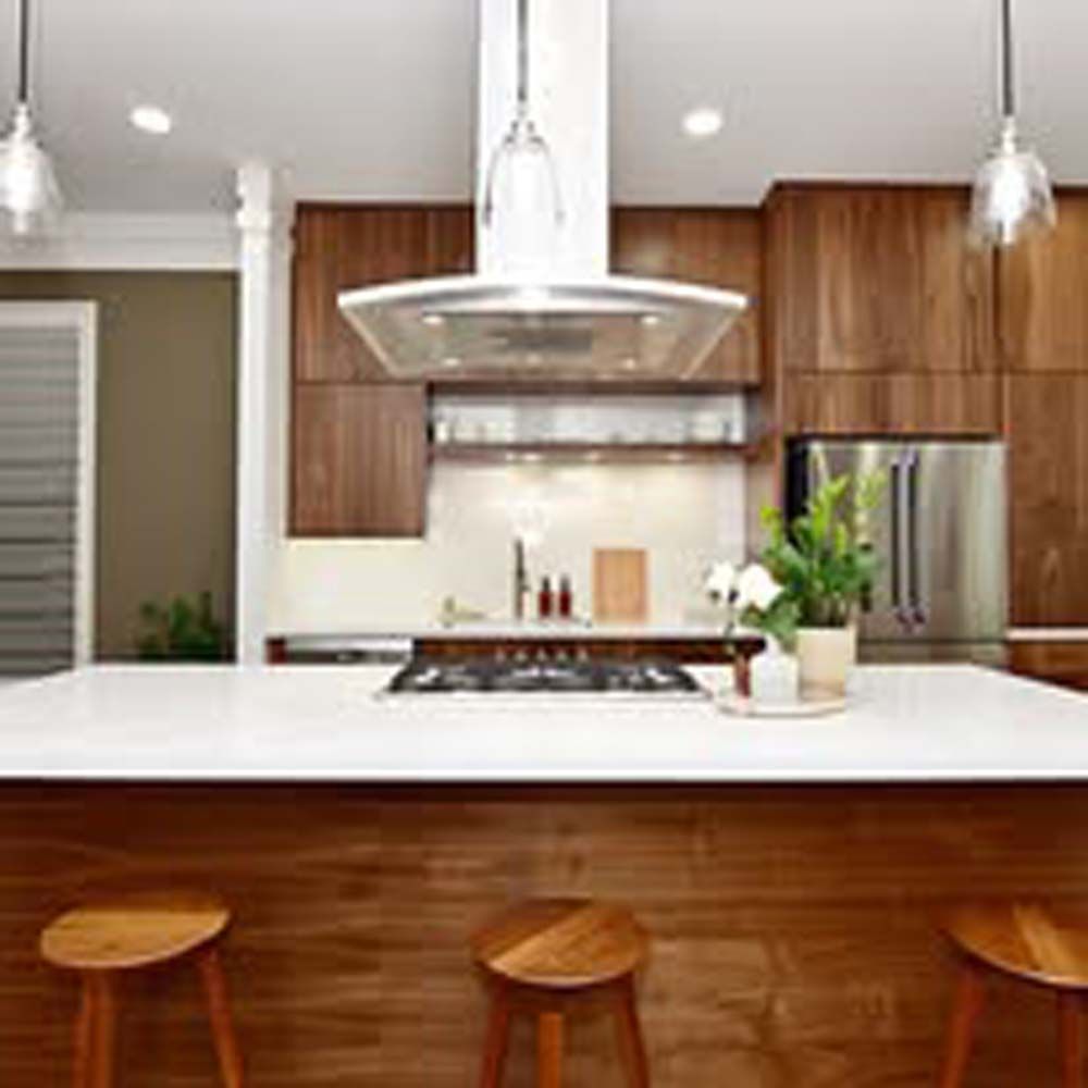 Modern kitchen with wood cabinets, white countertop, range hood, and stools.