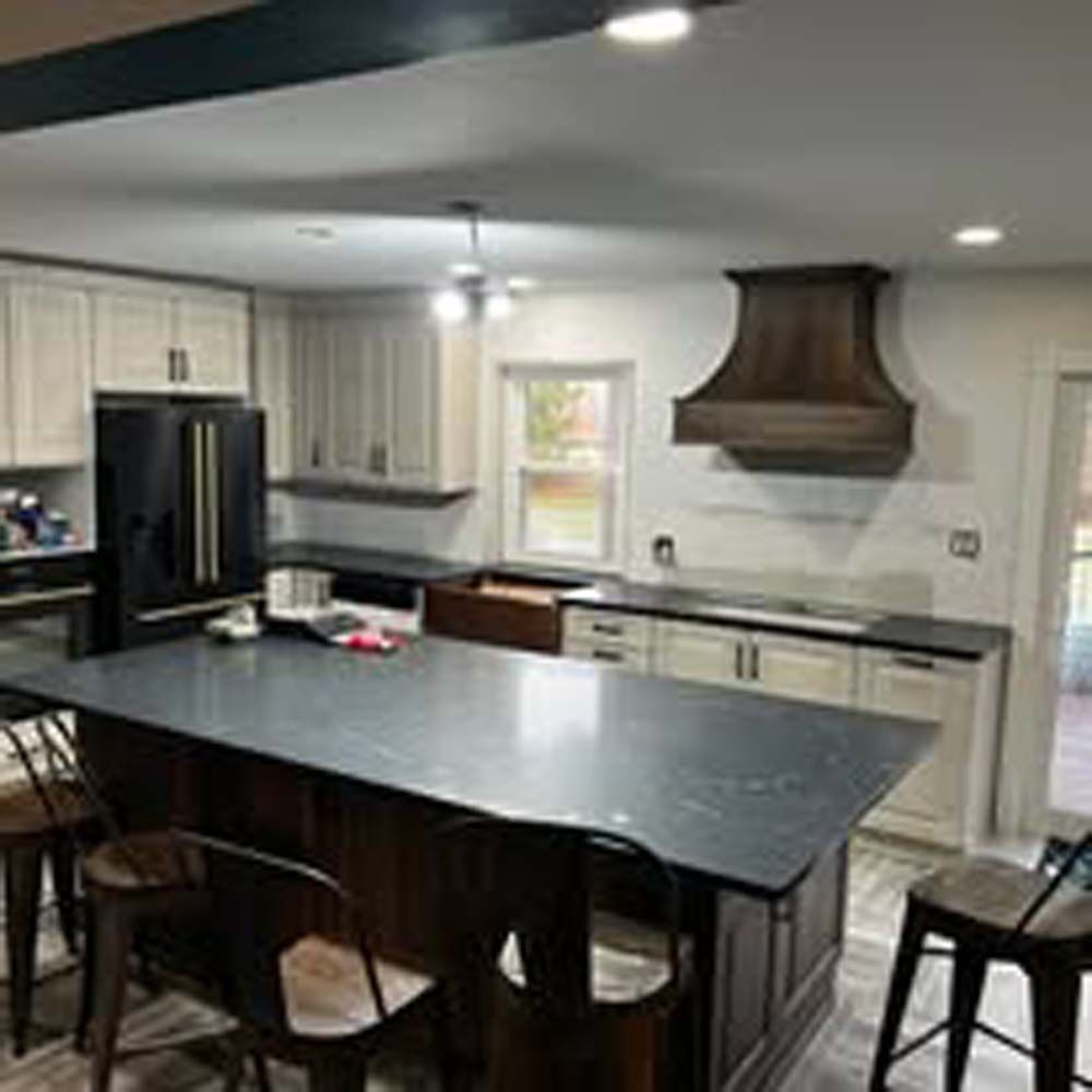 Kitchen with a dark island, light cabinets, and a wooden range hood.