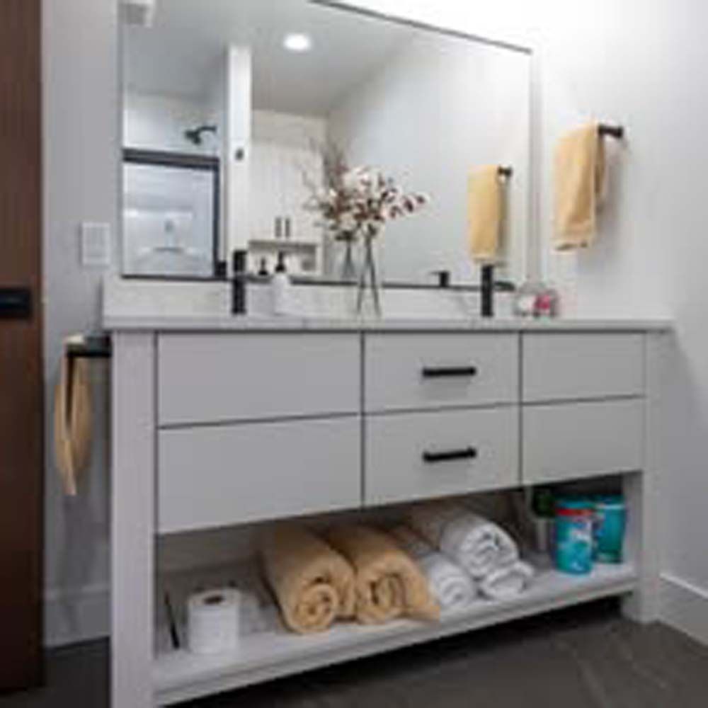 Bathroom vanity with double sinks, mirror, and towels. White cabinetry, black hardware.