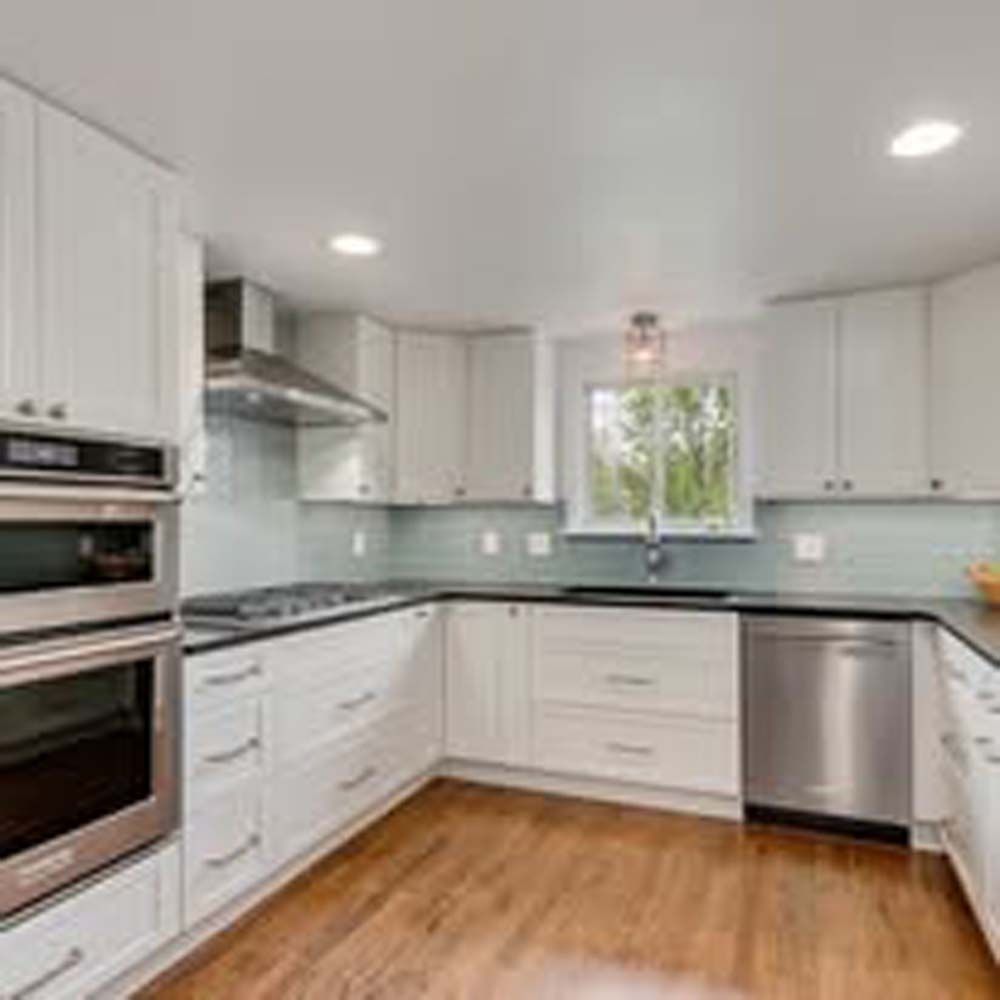 White kitchen with stainless steel appliances, wood floor, and window.
