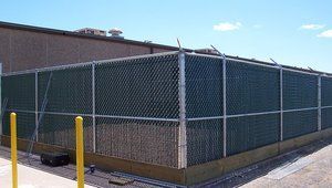 A chain link fence with a green slat is surrounding a building.