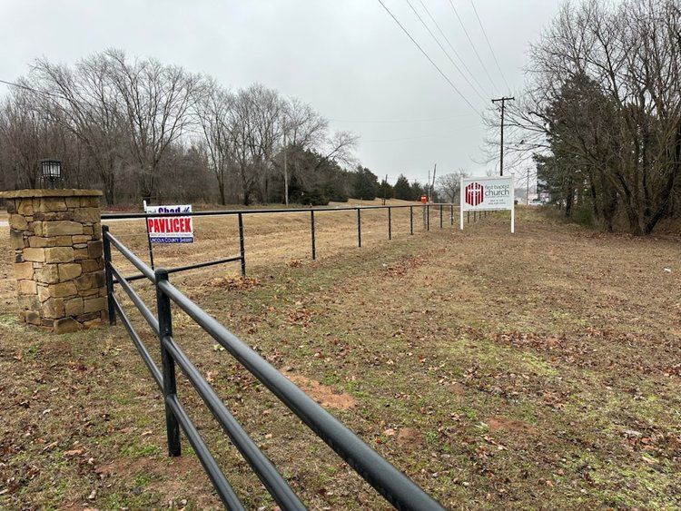 A fence surrounds a field with a for sale sign in the background.