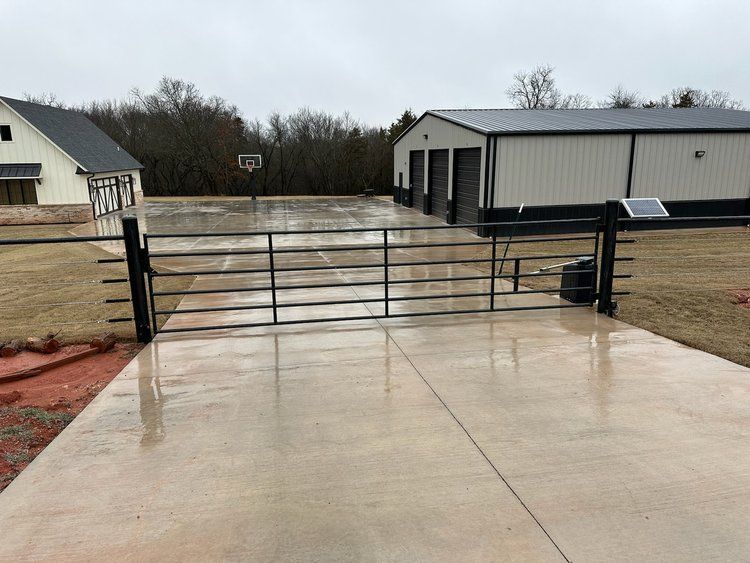 A concrete driveway with a gate and a basketball court in the background.