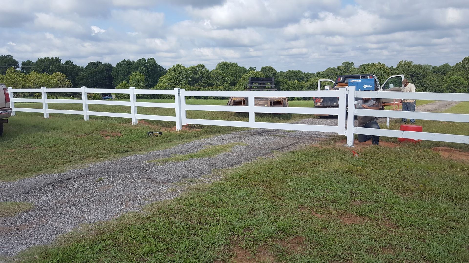 A white fence surrounds a dirt road in a grassy field
