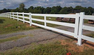 A white fence surrounds a dirt road in a field.