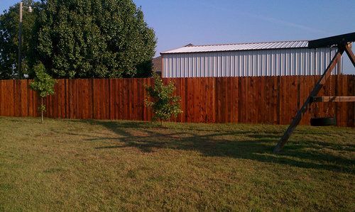 A wooden fence surrounds a lush green yard with a swing set in the background.