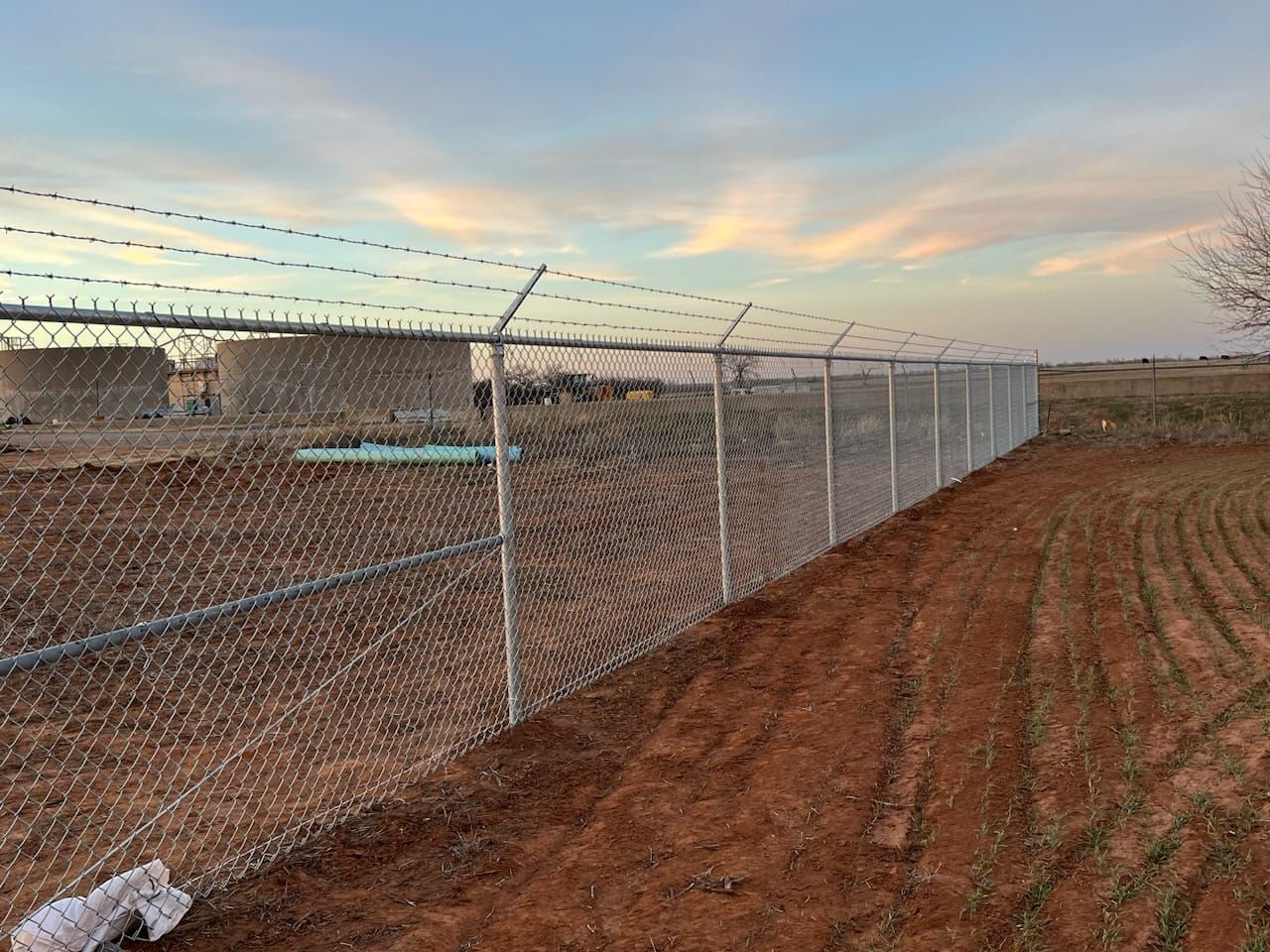A chain link fence is surrounding a field with barbed wire