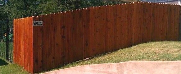 A wooden fence is sitting on top of a lush green field next to a driveway.