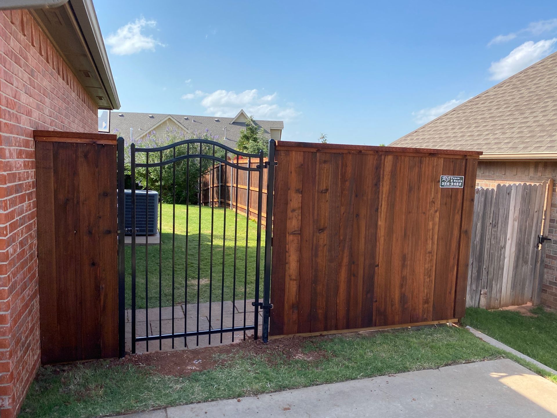 A wooden fence with a metal gate in front of a brick house