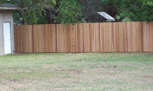 A wooden fence surrounds a lush green yard in front of a house.