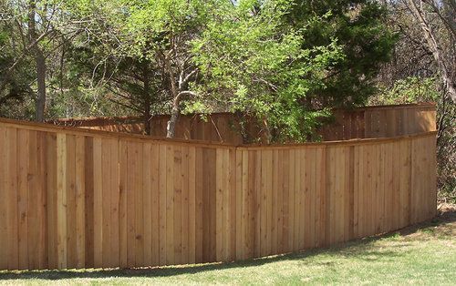 A wooden fence is surrounded by trees in a backyard.