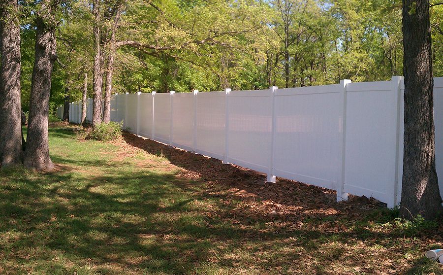 A white fence is surrounded by trees in a yard.