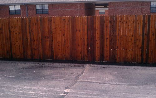 A wooden fence surrounds a parking lot in front of a brick building.
