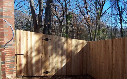 A wooden fence is surrounded by trees and a brick wall.