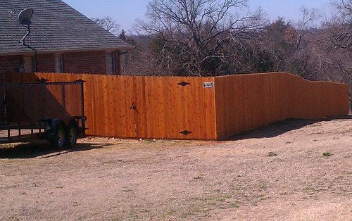 A wooden fence is surrounding a trailer in a dirt field.