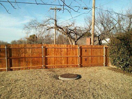 A wooden fence surrounds a gravel yard with a manhole cover in the middle.
