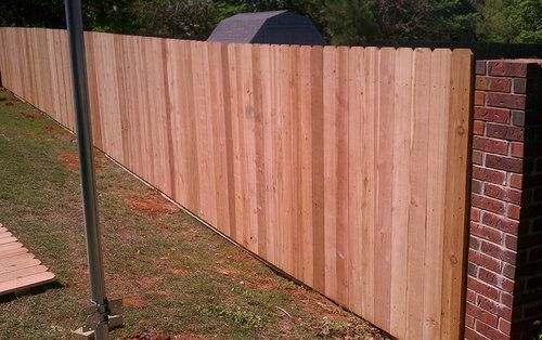 A wooden fence surrounds a brick wall in a yard.