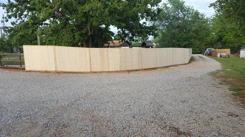 A wooden fence is sitting on the side of a gravel road.