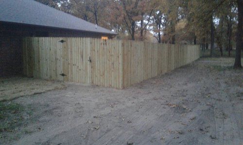 A wooden fence is along the side of a dirt road next to a house.