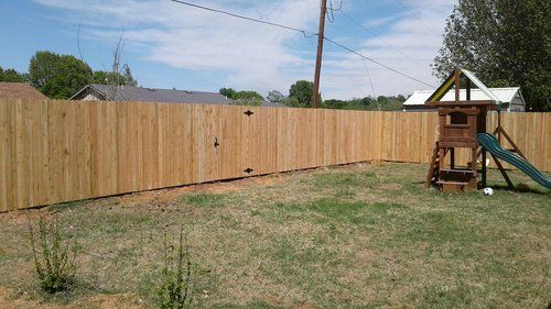 A wooden fence surrounds a playground in a backyard.