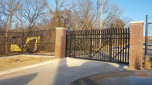 A black gate with a brick pillar and a yellow excavator in the background.