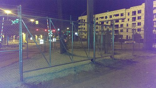 A chain link fence with a building in the background at night