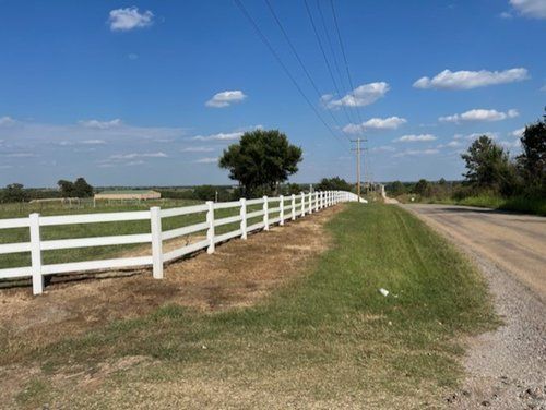A white fence along the side of a dirt road.