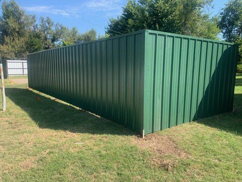 A green metal fence is sitting in the middle of a grassy field.
