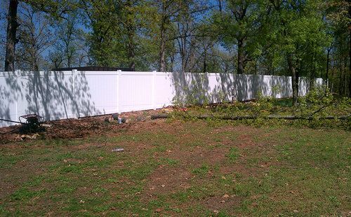 A white fence surrounds a grassy field with trees in the background.