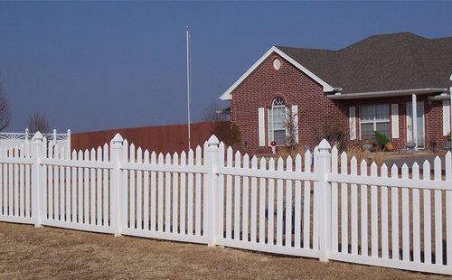 A white picket fence surrounds a brick house