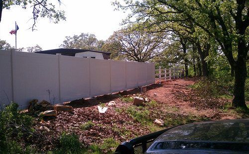 A white fence surrounds a dirt road in front of a house.