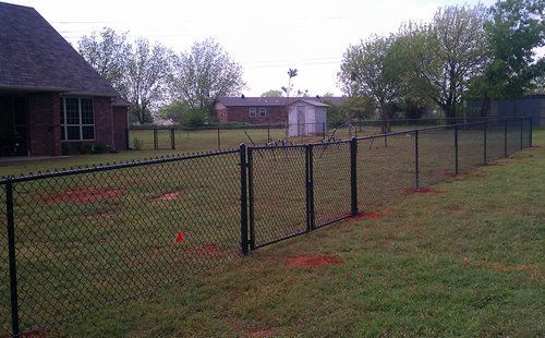 A chain link fence surrounds a grassy yard in front of a house.