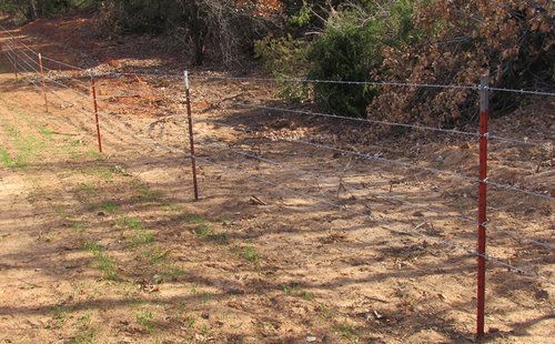 A barbed wire fence is surrounding a dirt field.
