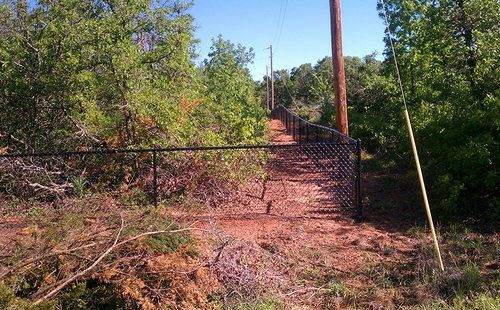 A chain link fence is surrounded by trees and dirt