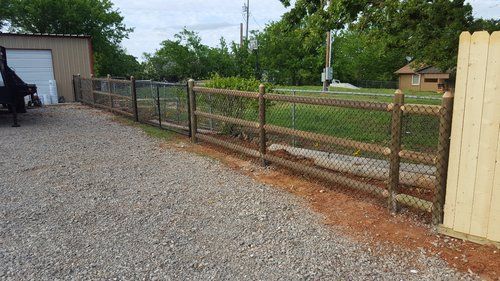 A wooden fence surrounds a gravel driveway next to a garage.