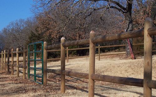 A wooden fence surrounds a playground with trees in the background.