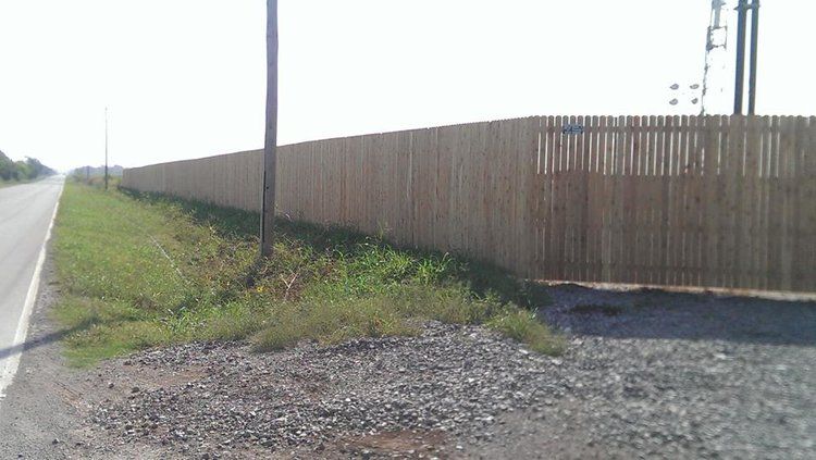 A large wooden fence is along the side of a road.