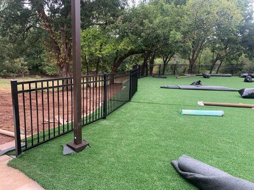 A fence surrounds a lush green field of artificial grass.