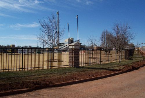 A fence surrounds a field with a stadium in the background.