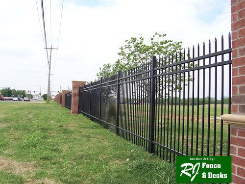 A black metal fence surrounds a grassy field next to a brick wall.