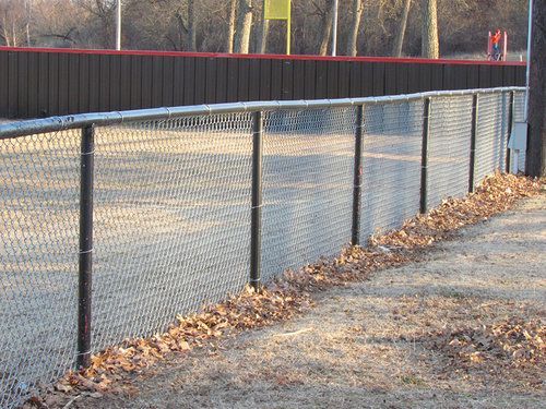 A chain link fence with leaves on the ground