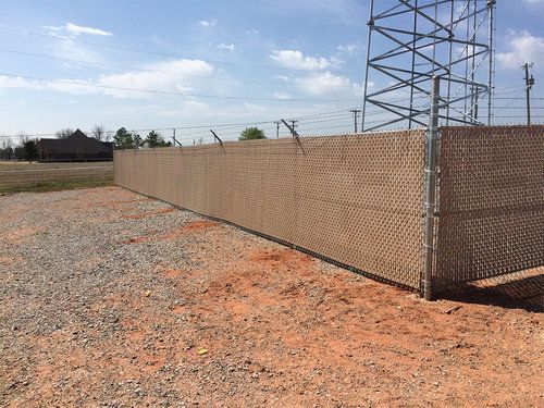 A chain link fence is surrounding a gravel area with a power tower in the background.