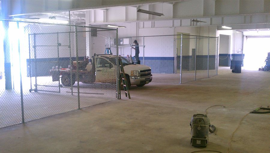 A white truck is parked in a garage behind a chain link fence.
