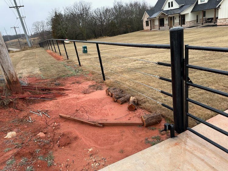 A black metal fence surrounds a dirt area in front of a house.