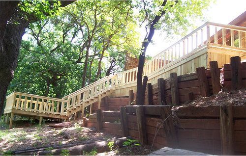 A wooden deck with stairs leading up to it is surrounded by trees.