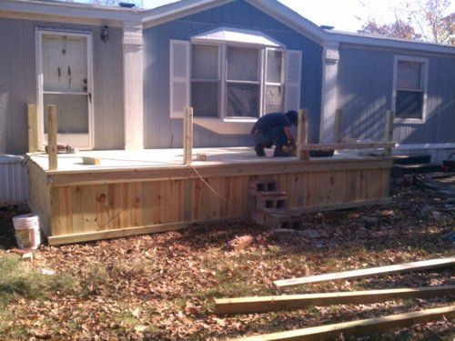 A man is working on a wooden deck in front of a mobile home